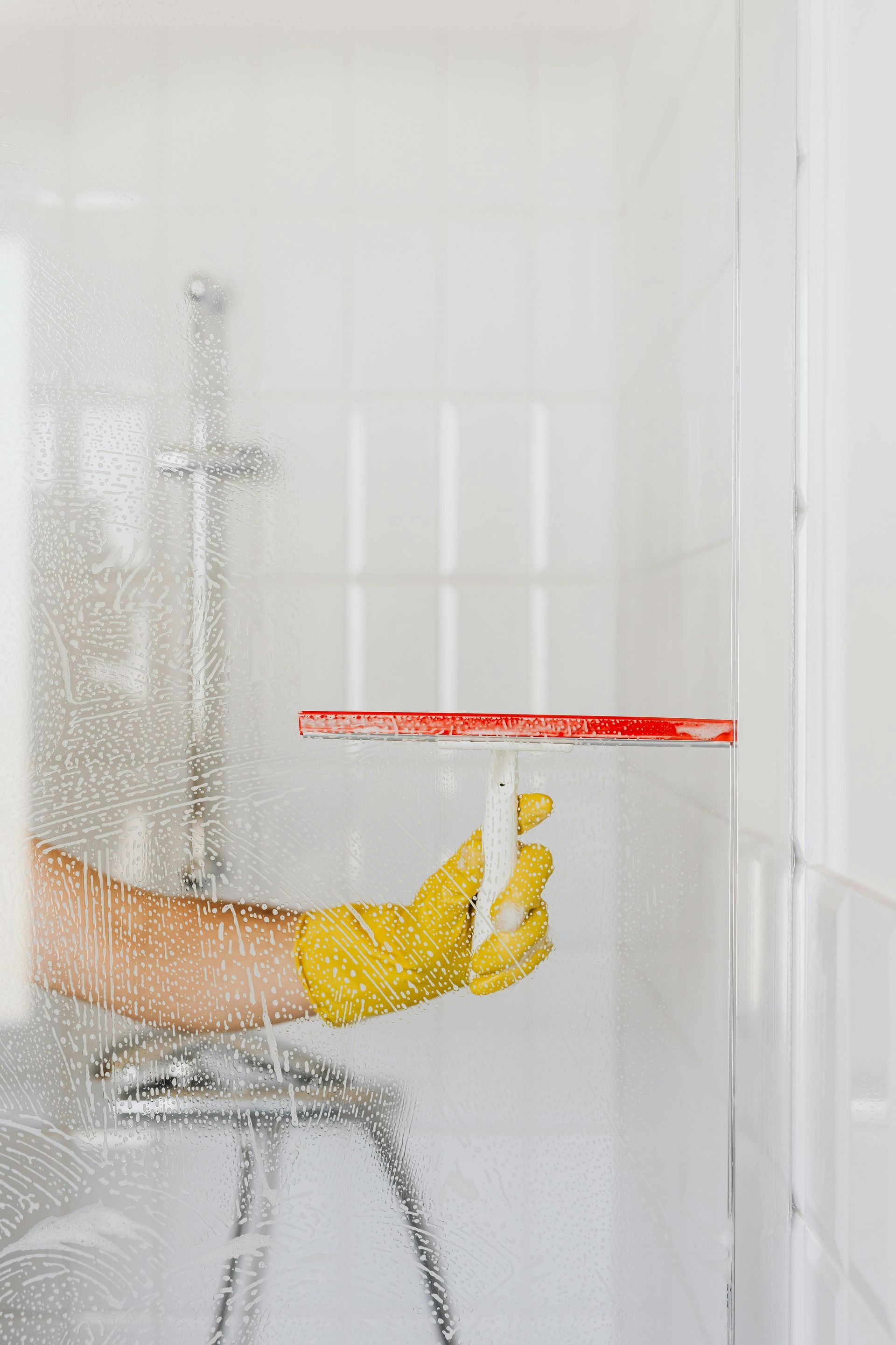 Person wearing yellow glove squeegees soapy shower door.
