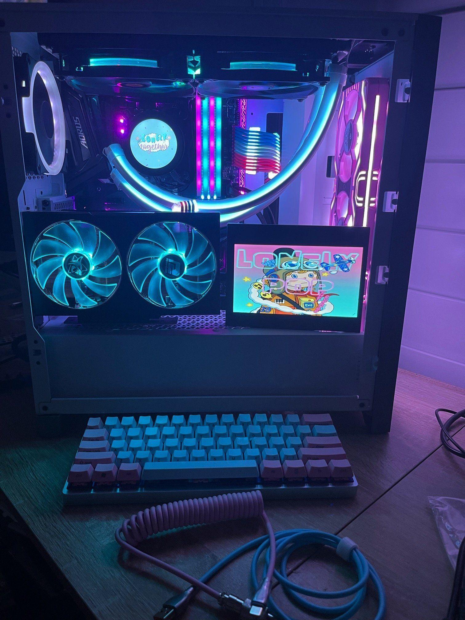 A custom PC rig with bright blue and pink lighting, a small display showing colorful art, and a keyboard.