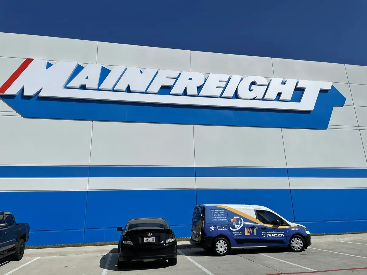 Mainfreight building with large blue and white sign, parked cars in front, including a blue service van.