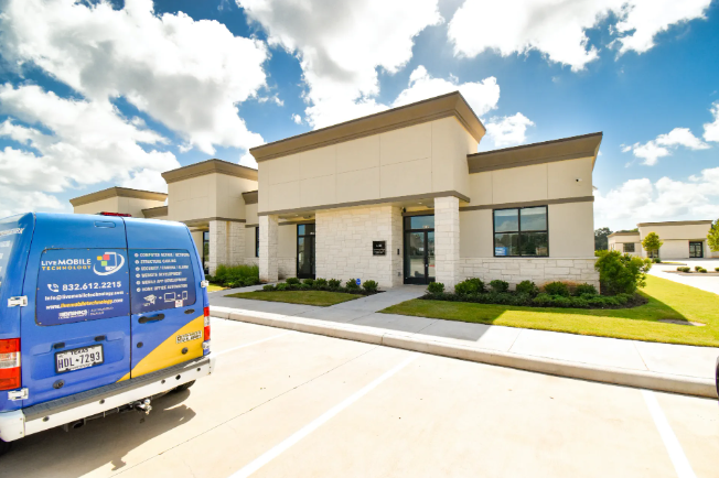 A blue and yellow service van parked in front of a beige commercial building on a sunny day.