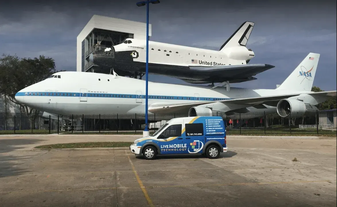 A large white airplane and the Space Shuttle on display at a museum, with a service van in the foreground.