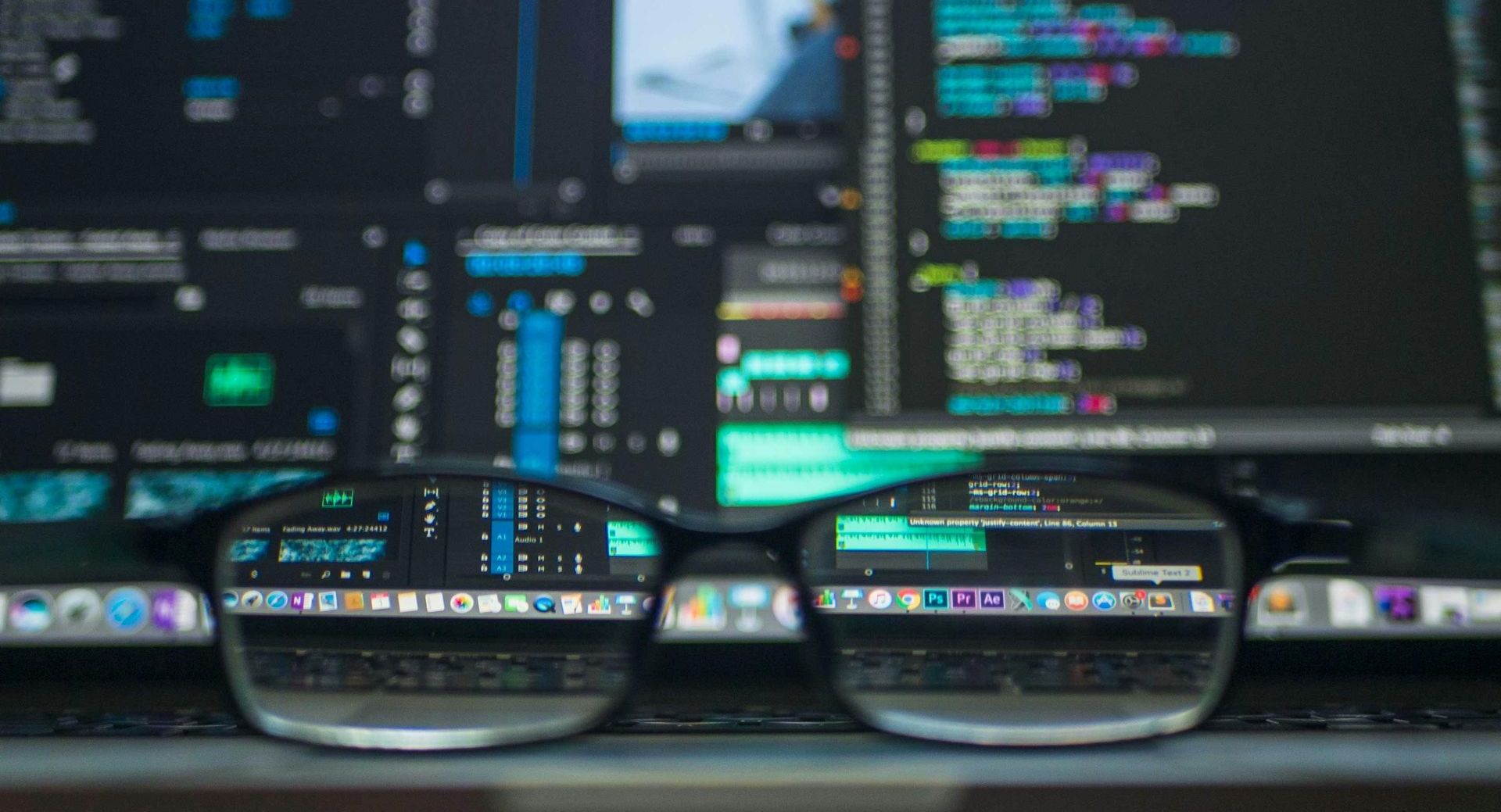 Glasses reflecting a computer screen with code, sitting on a laptop displaying multiple app icons.