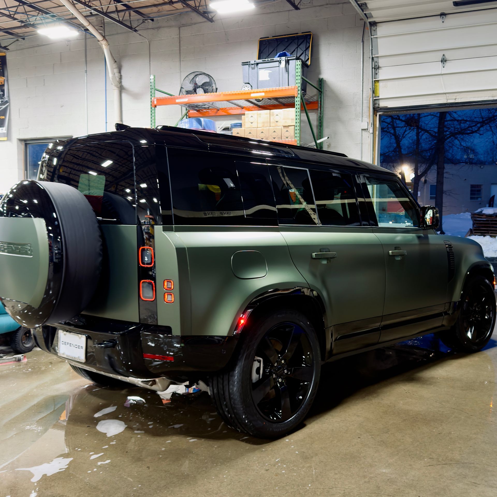 Matte green off-road SUV parked in a garage, viewed from the rear-left side.