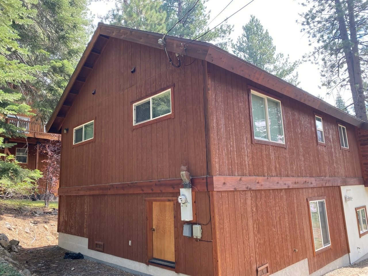 Two-story brown wooden cabin with white-trimmed windows in a wooded area