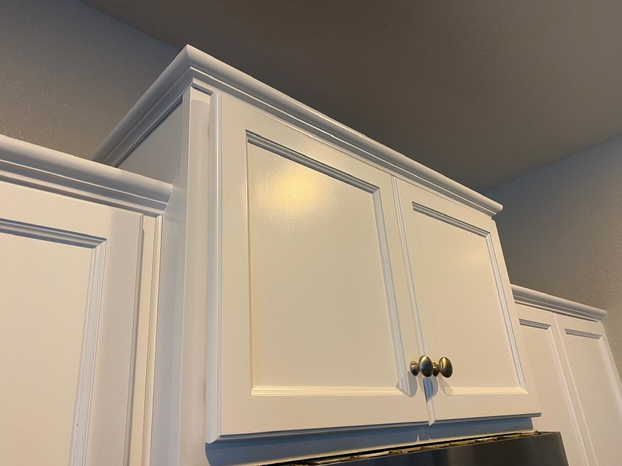 White kitchen cabinets with silver knobs against a beige wall, viewed from below