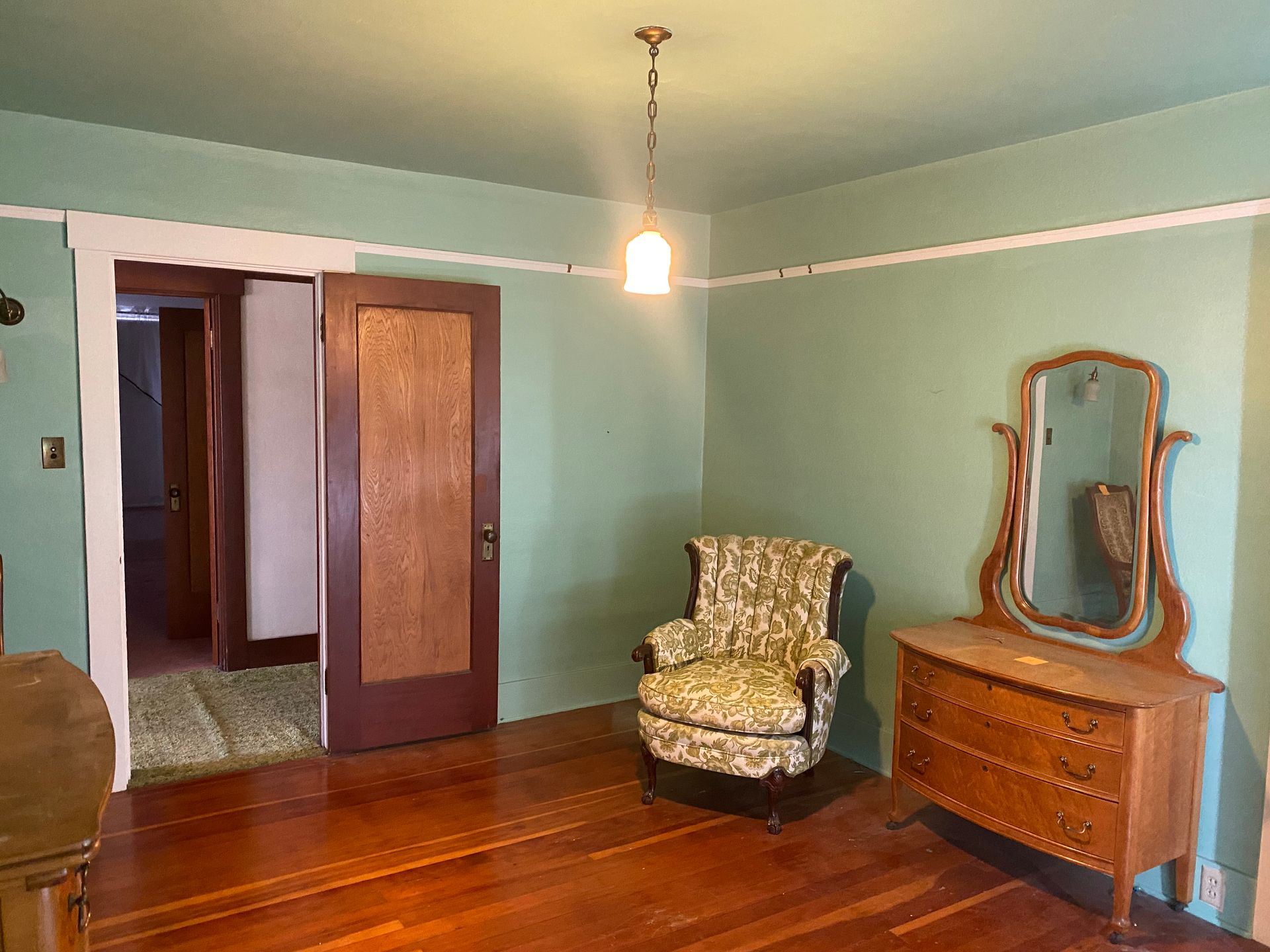 Vintage bedroom with mint green walls, wooden floor, wardrobe, armchair, and dresser with mirror