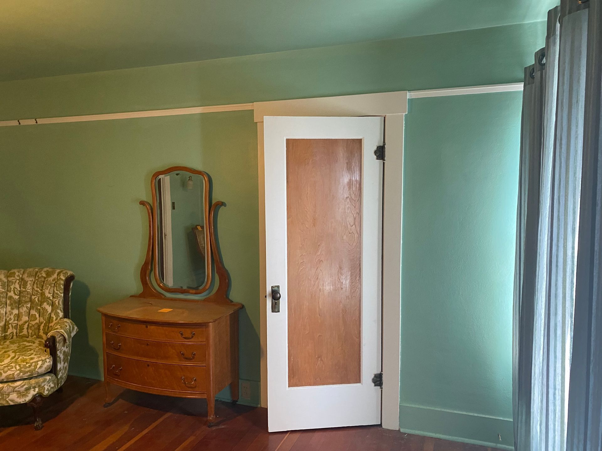 Green bedroom with a wooden dresser and mirror beside a white door on teal walls