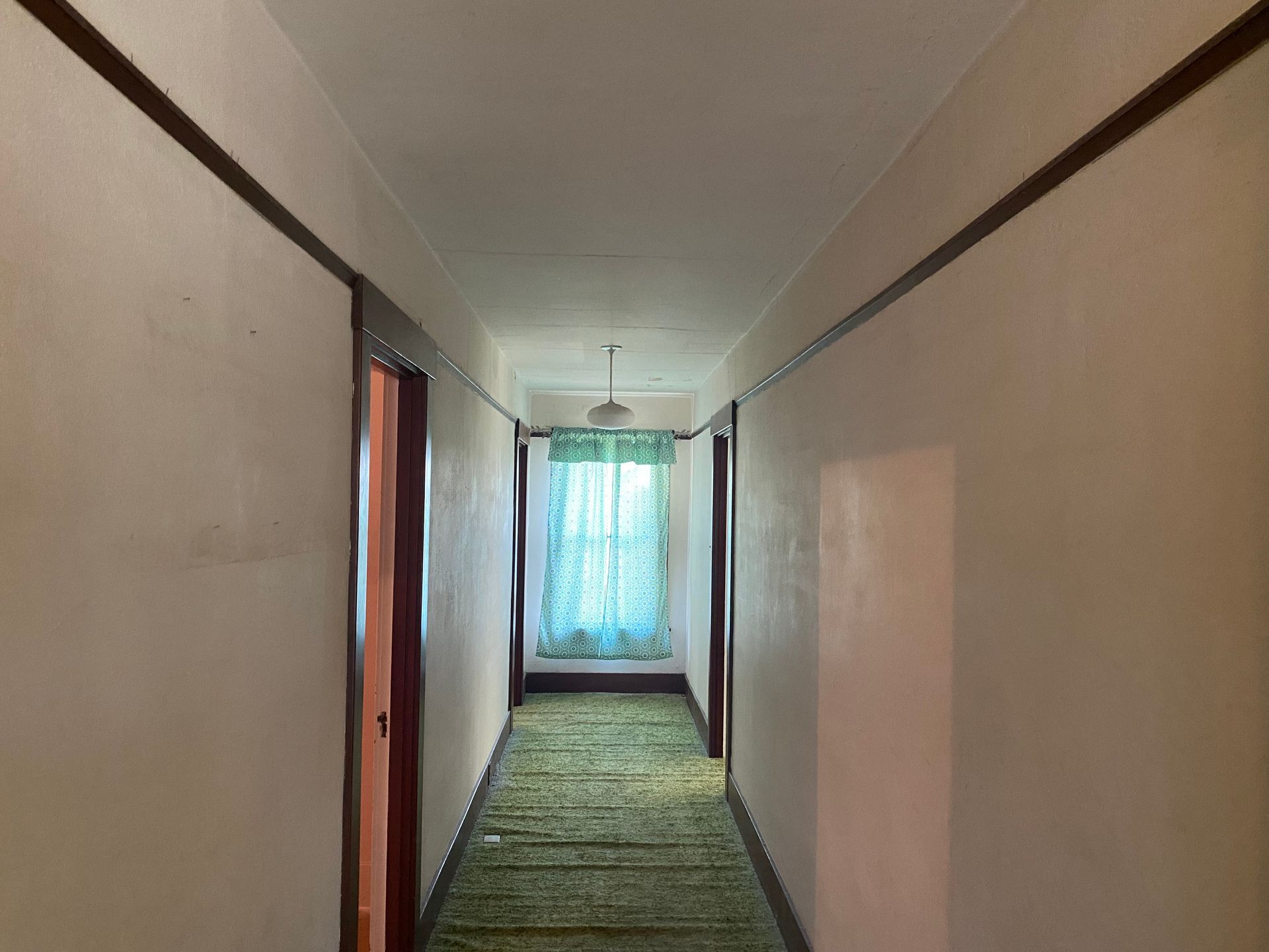 Narrow hallway with beige walls, green carpet, and a bright turquoise curtain at the far end.