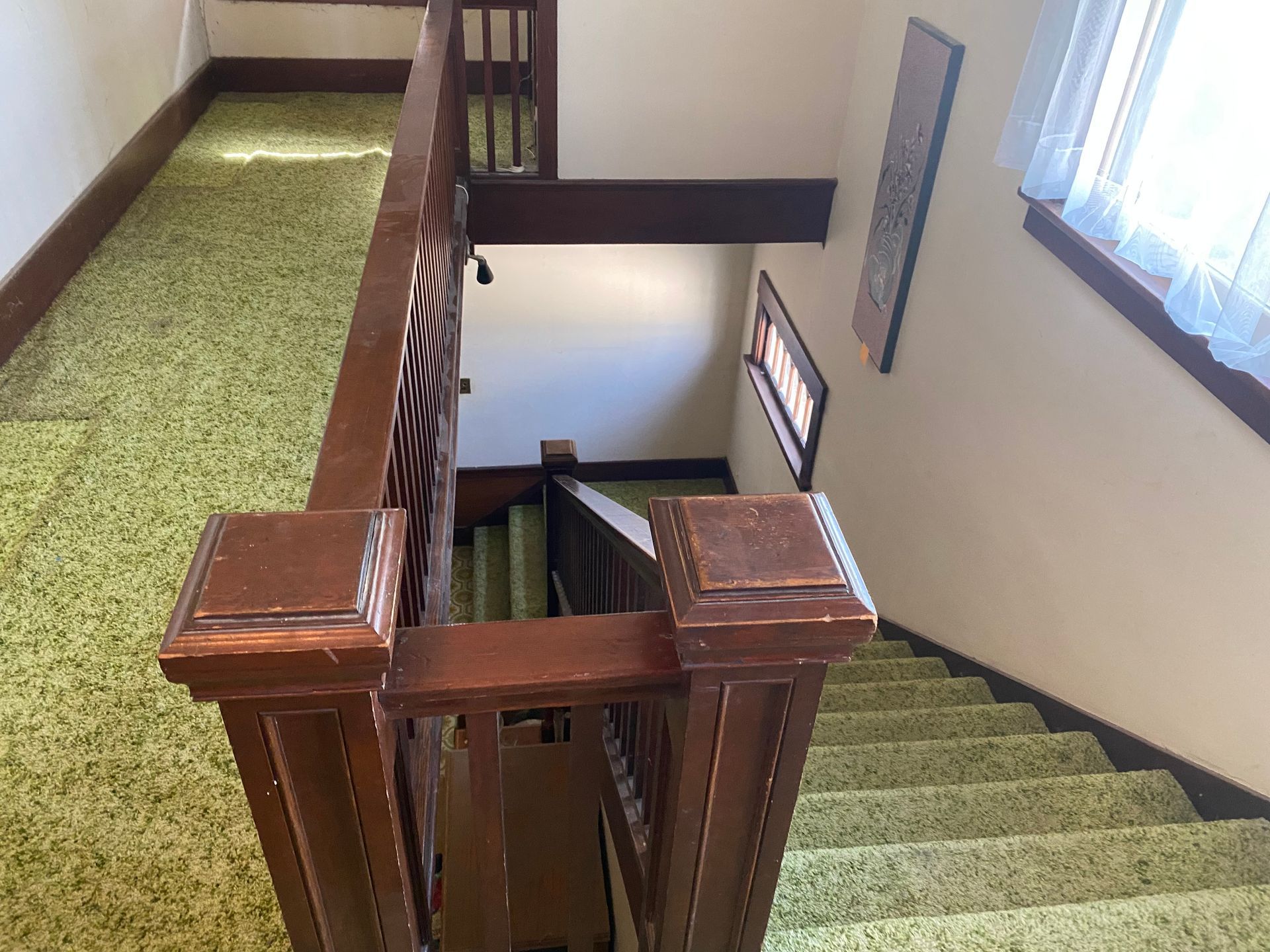 Indoor stairwell with green carpeted stairs and wooden railing beside a windowed landing.