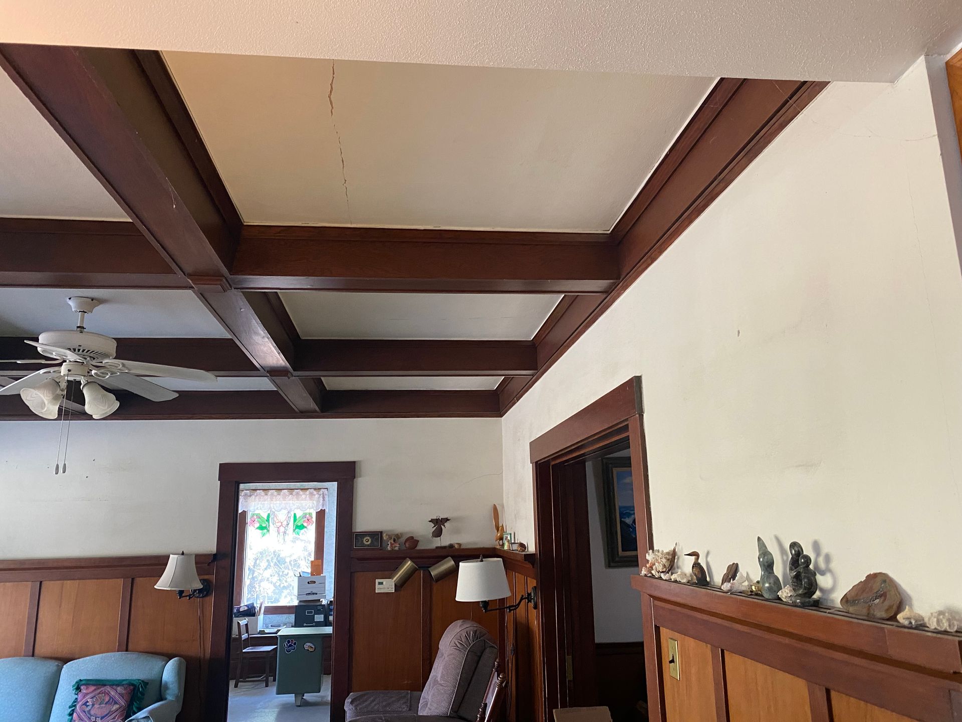 Living room with exposed wooden ceiling beams, white walls, and a doorway leading outside.
