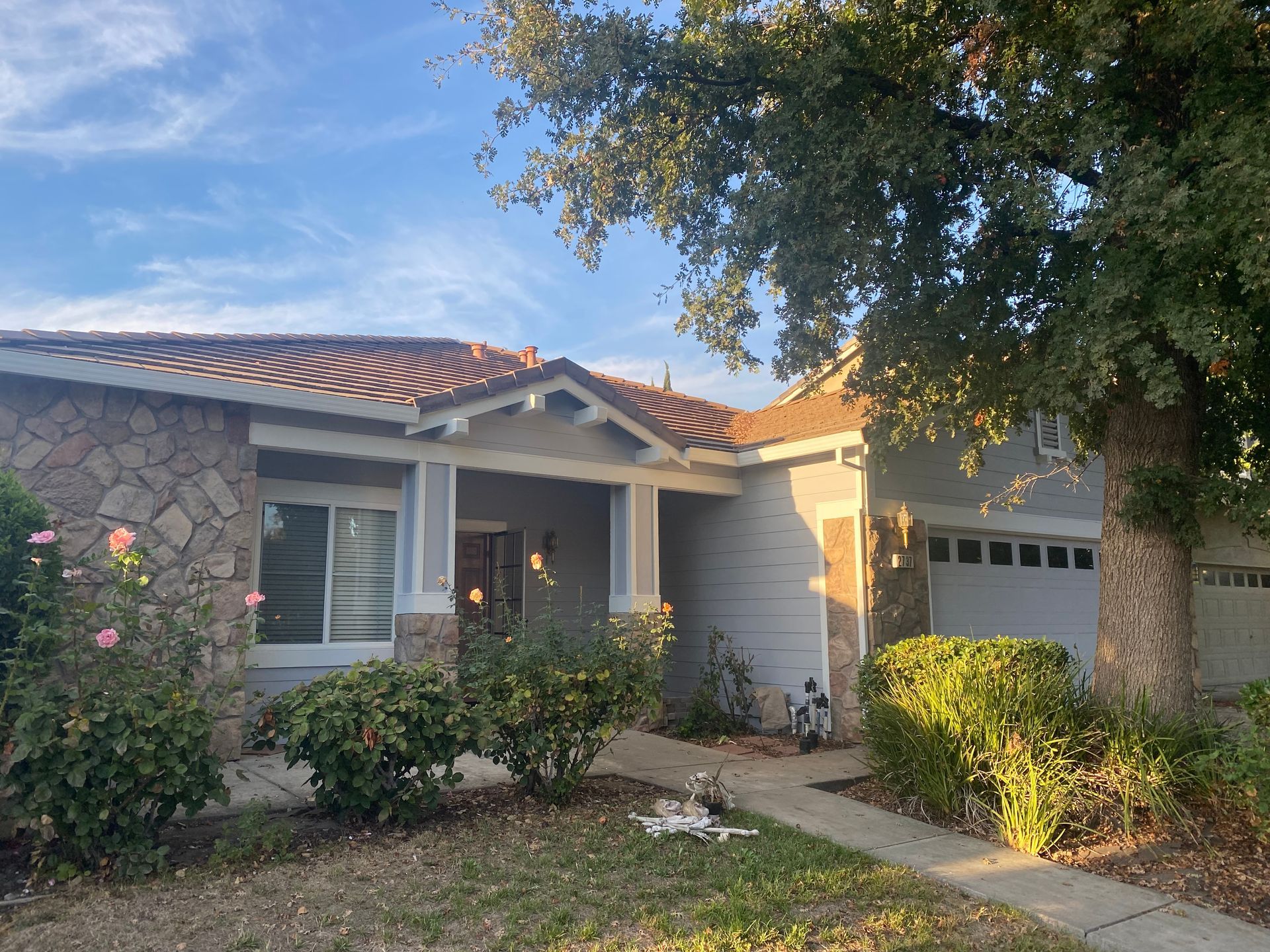 Single-story stucco house with red tile roof, front porch, and a garage under a blue sky.