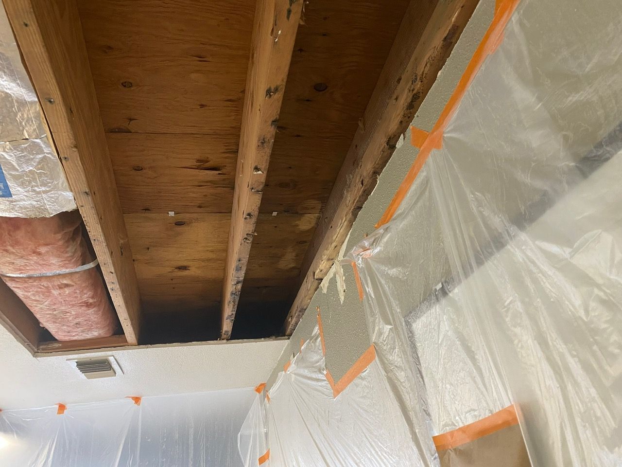 Partially exposed ceiling joists and insulation during home renovation, with plastic sheeting and orange tape