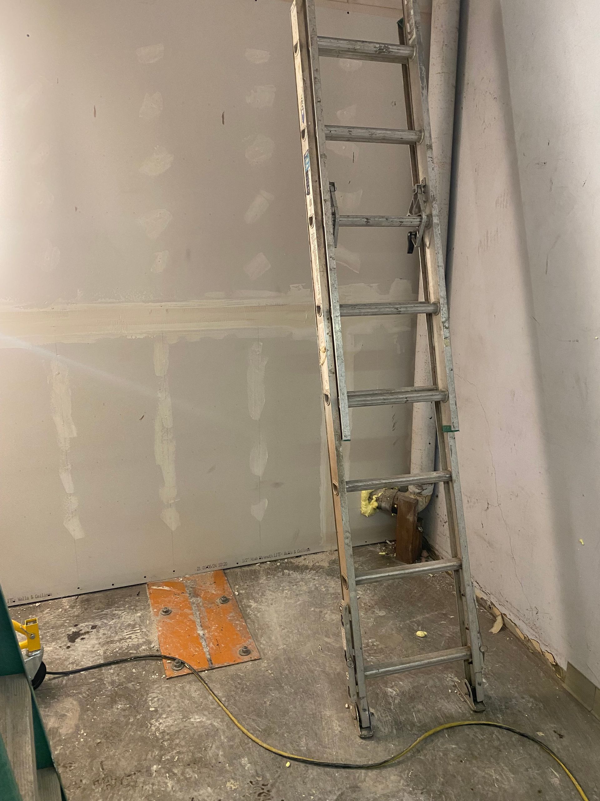 Metal ladder leaning against a plastered wall in an unfinished room with construction debris on the floor