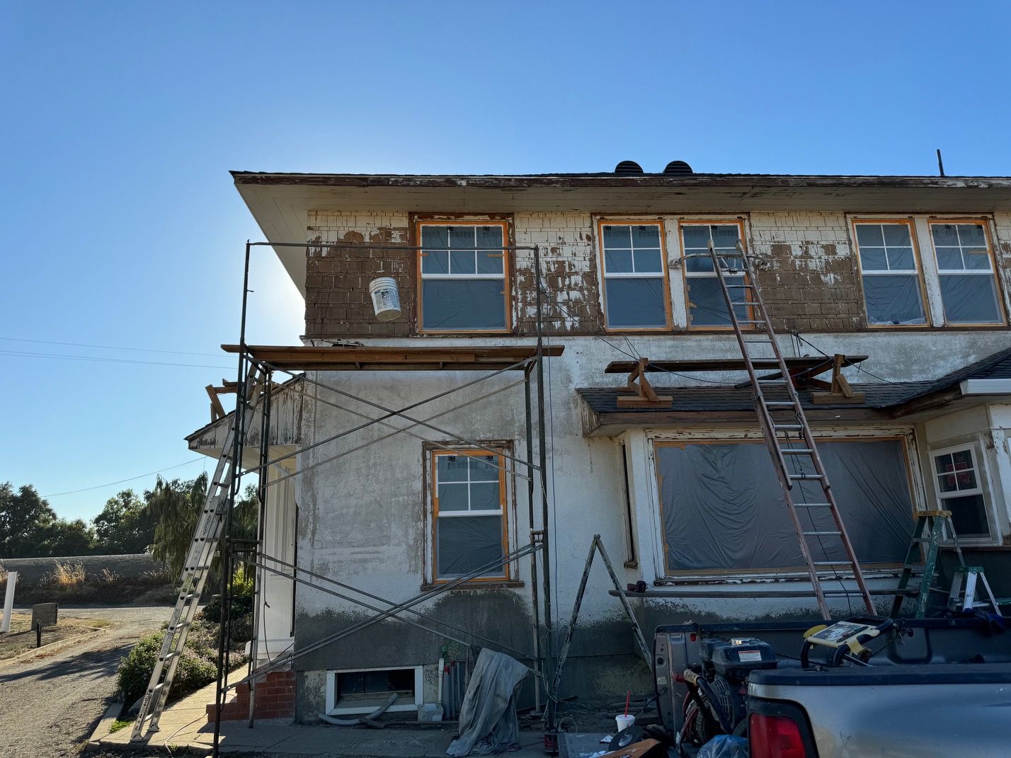 Dilapidated two-story building with peeling paint, scaffolding, and a ladder under a clear blue sky