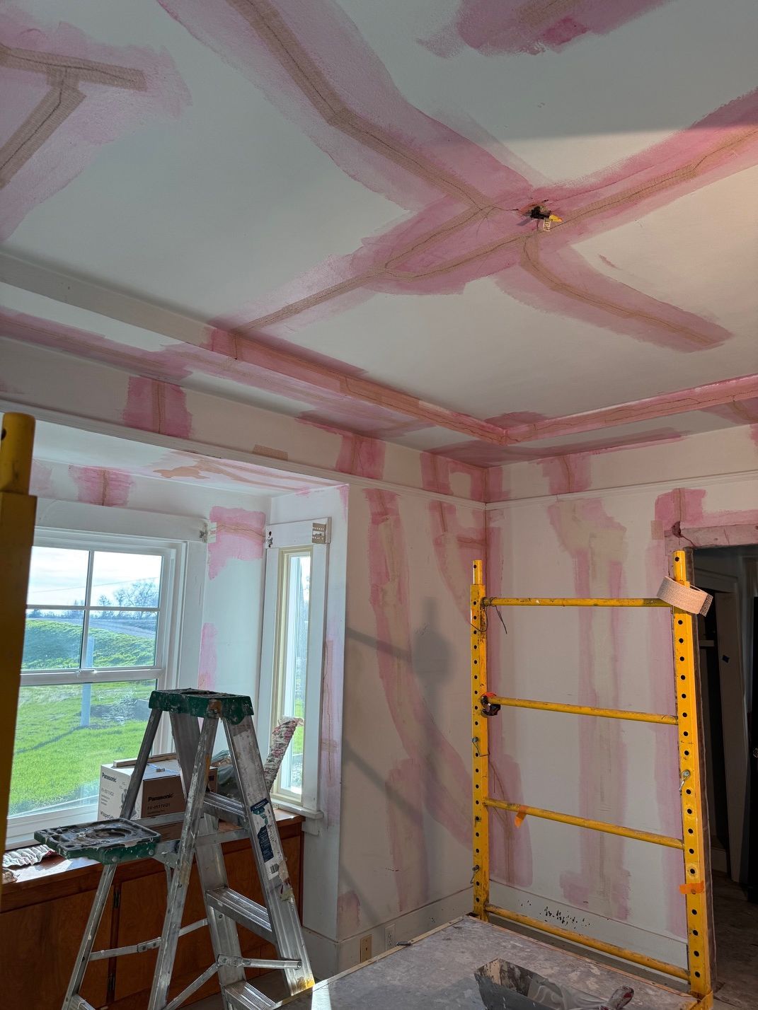 Partially renovated room with drywall seams, ladders, and a yellow scaffold by a window