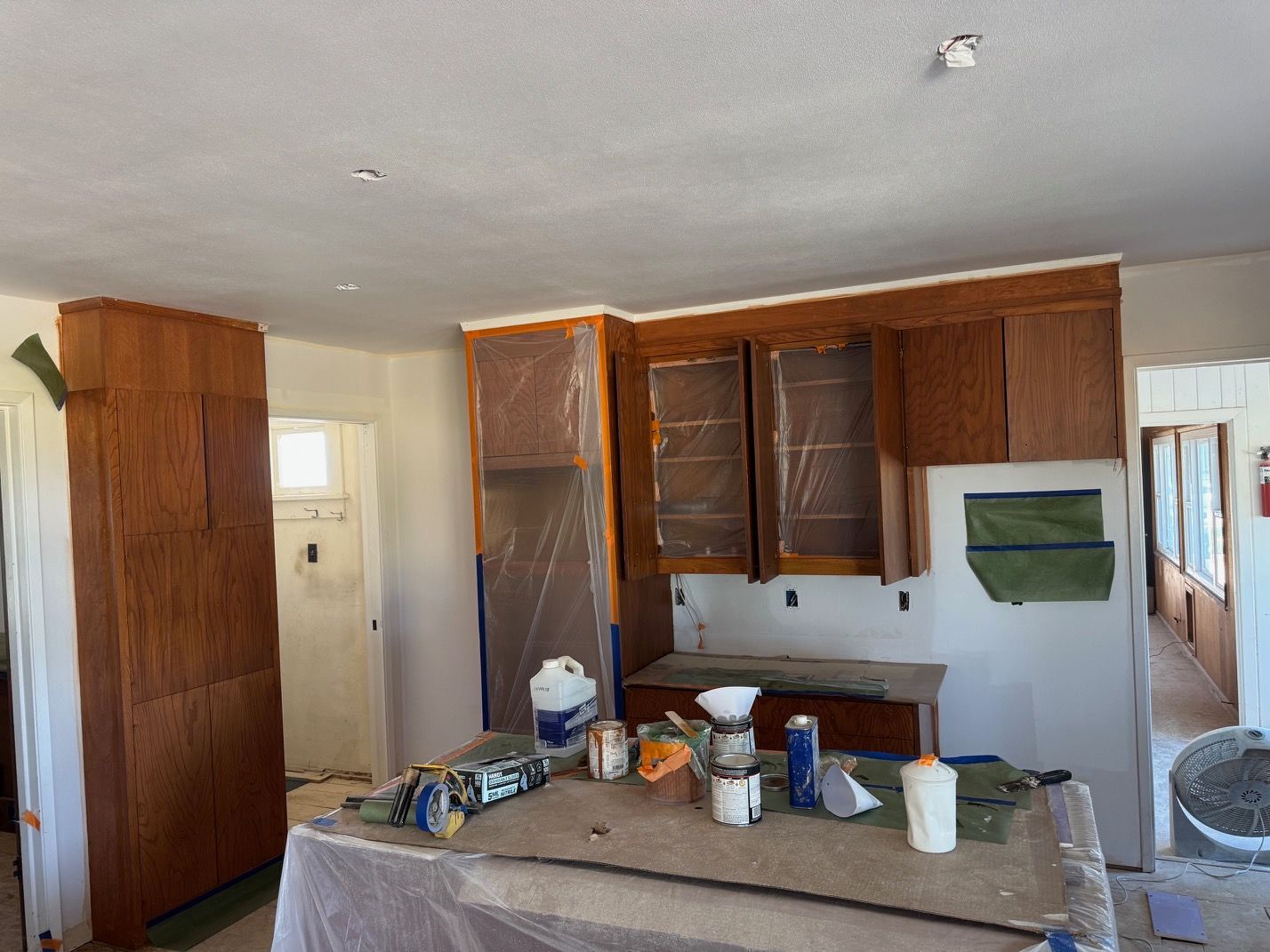 Partially renovated kitchen with cabinets covered in plastic and tools on a central island