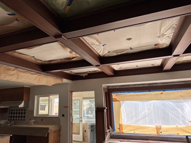 Damaged ceiling with exposed wooden beams in a room under renovation, light coming through covered windows