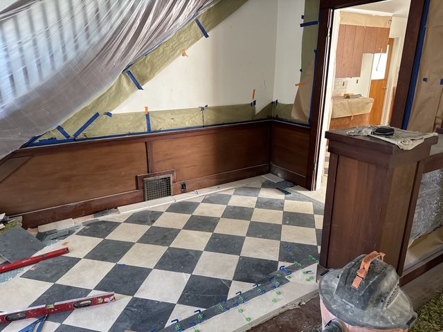 Partially renovated room with checkered floor, wood paneling, and plastic sheeting over walls and windows