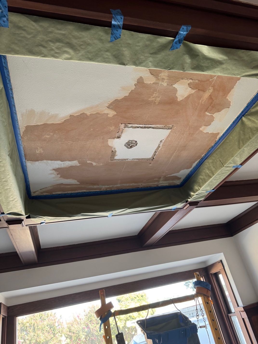 Peeling ceiling patch with taped edges above a window in an interior room