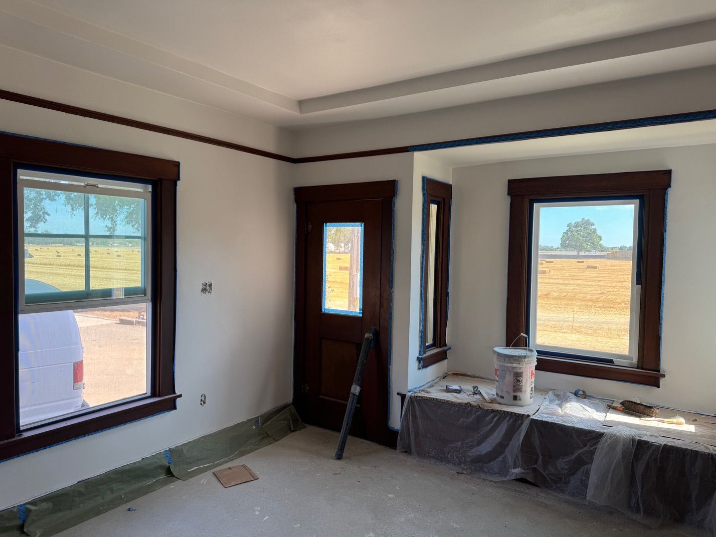 Empty room under renovation with three windows, white walls, and a covered table by the wall