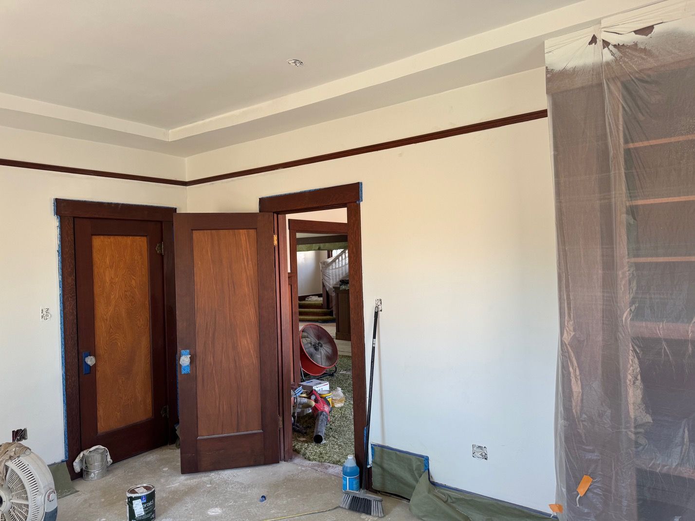 Empty room with cream walls, dark wood doors, and construction materials near a covered doorway.