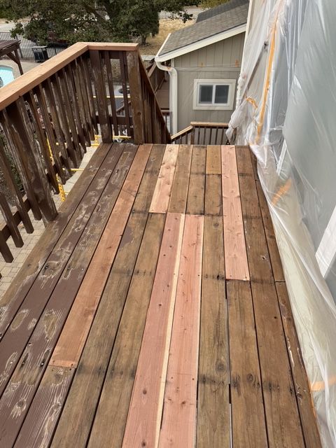 Weathered wooden balcony deck under renovation, with plastic sheeting along the right side.