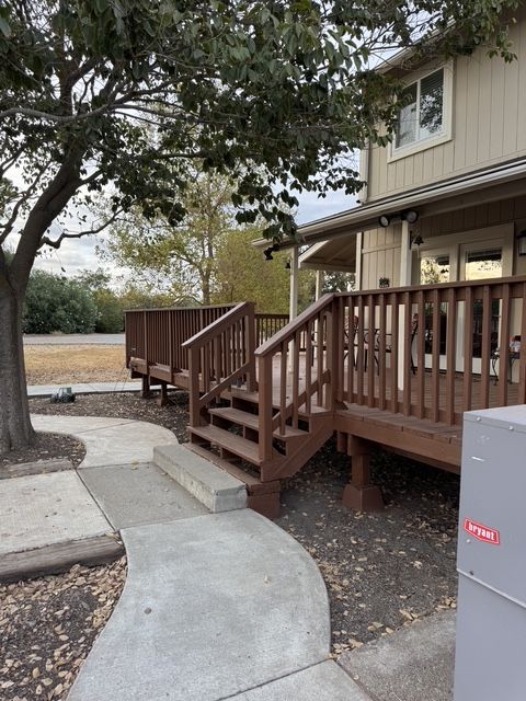 Curved concrete path leading to a wooden porch ramp and stairs beside a beige house and tree.