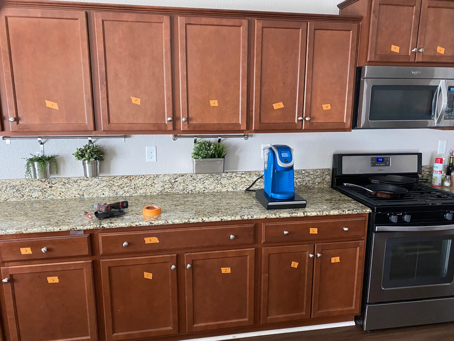 Kitchen with brown cabinets, speckled countertop, blue coffee maker, and stainless steel stove and microwave.