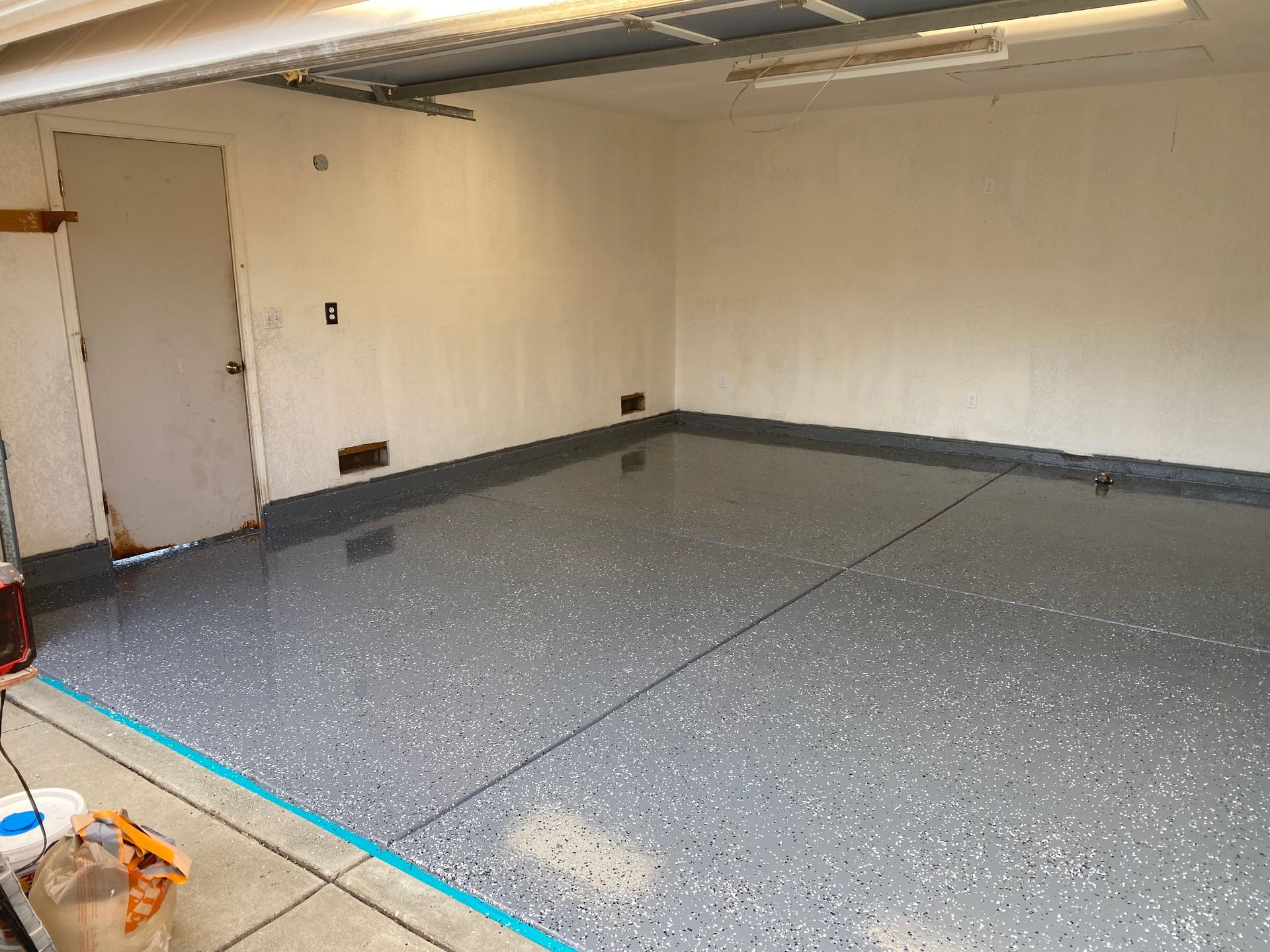 Empty beige garage with gray speckled floor and a closed door on the left.