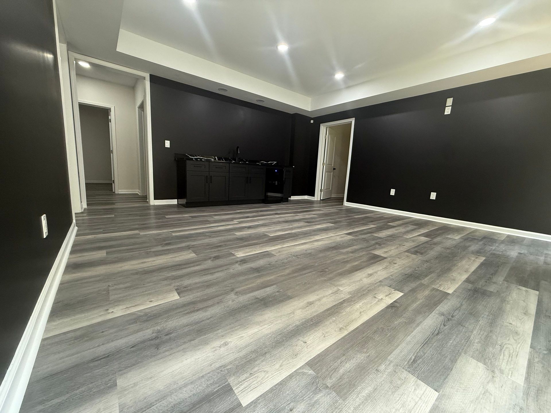 Empty room with gray wood-look flooring, black walls, white trim, and a built-in cabinet.