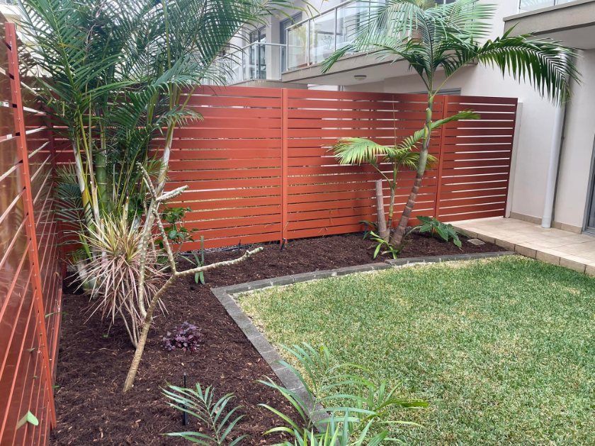 A Backyard With a Wooden Fence and a Lush Green Lawn — Greener Gardens Gardening Service In Lake Cathie, NSW
