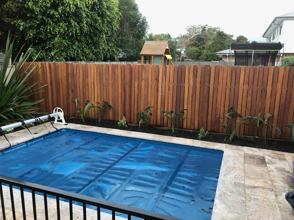 A Wooden Fence Surrounds a Swimming Pool in a Backyard — Greener Gardens Gardening Service In Thrumster, NSW