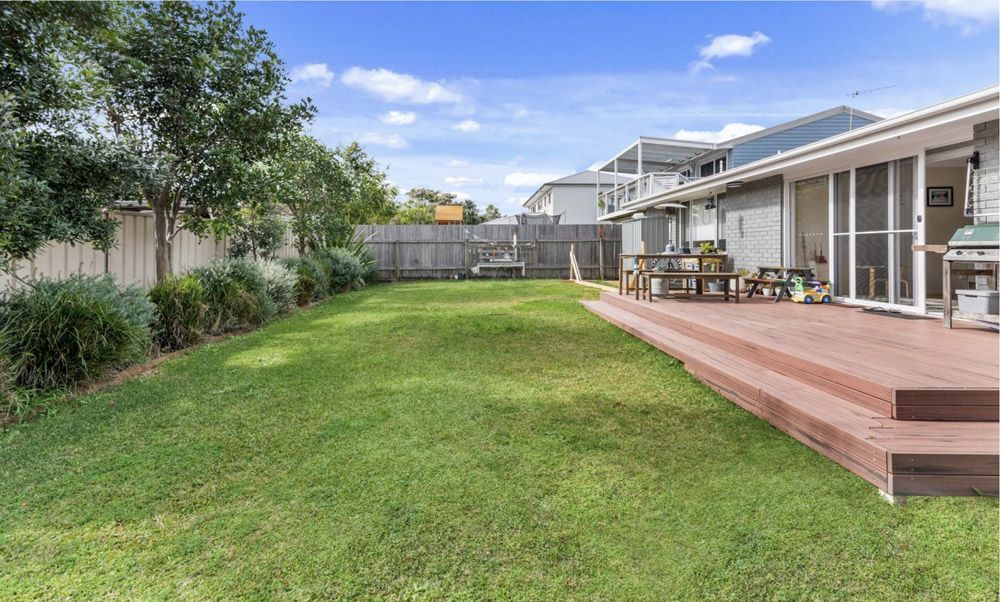 The backyard of a house with a large lawn and a wooden deck. — Greener Gardens Gardening Service In Thrumster, NSW
