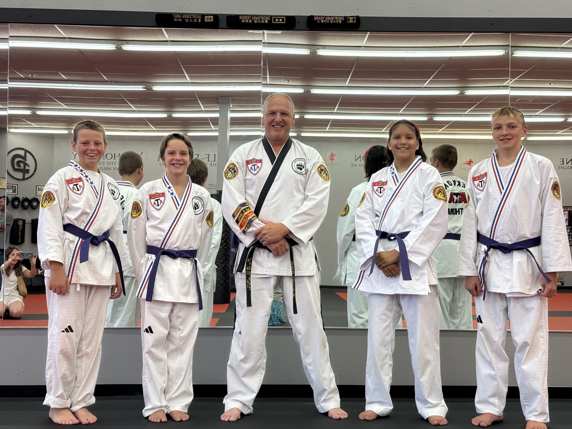 Five people in martial arts uniforms posing in front of a mirror.