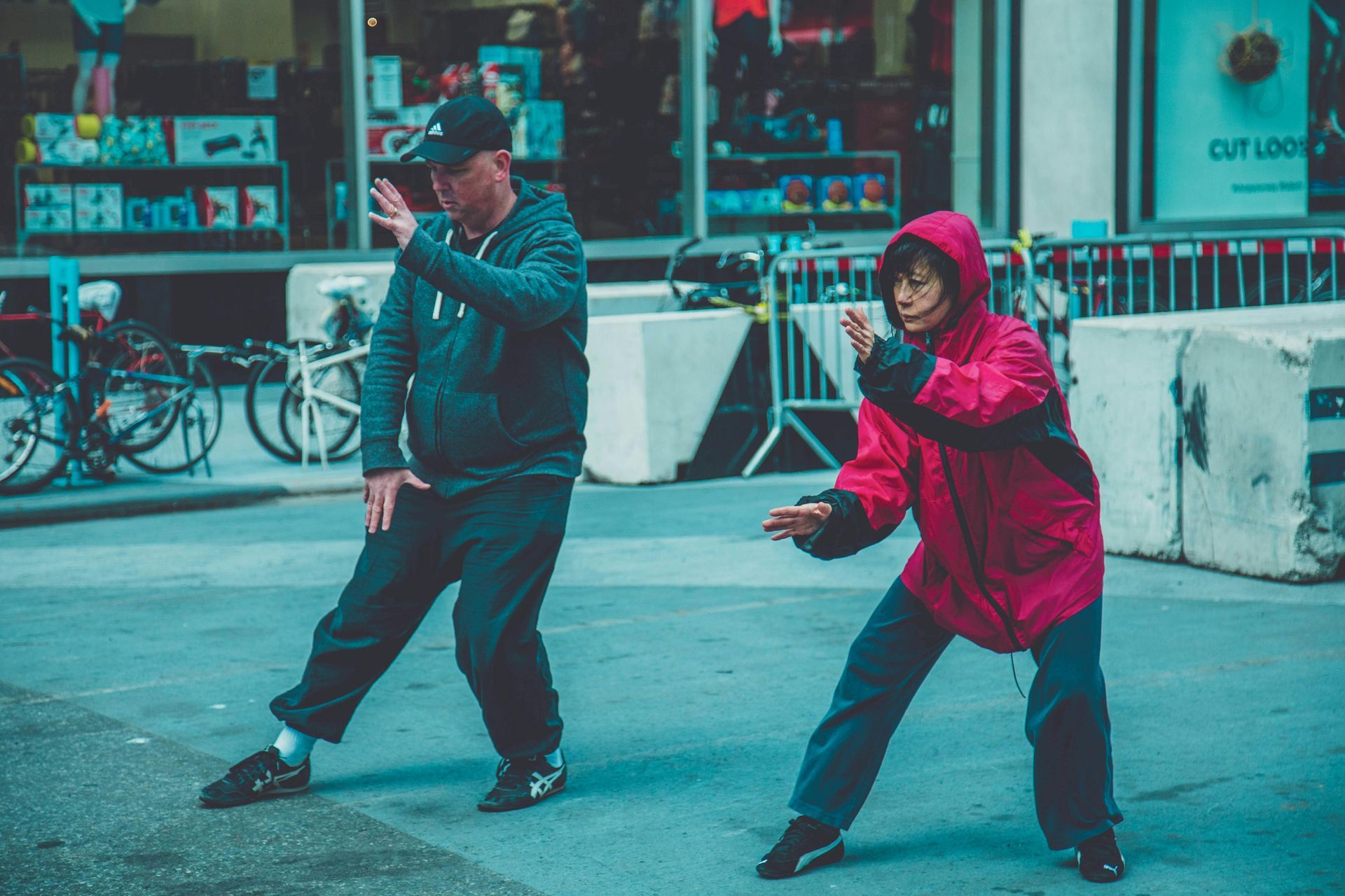 Two people practice Tai Chi on a city street. One in red, the other in blue.