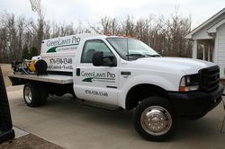 A white GreenLawn Pro work truck with specialized equipment is parked on a driveway in front of a house.
