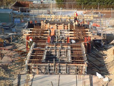 Construction workers on a concrete foundation with steel rebar and wooden formwork at a building site