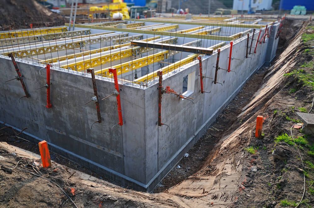 Concrete building foundation under construction with yellow formwork and red supports on a muddy site