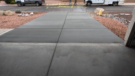 Concrete sidewalk leading to a parking lot, bordered by rocks and a curb