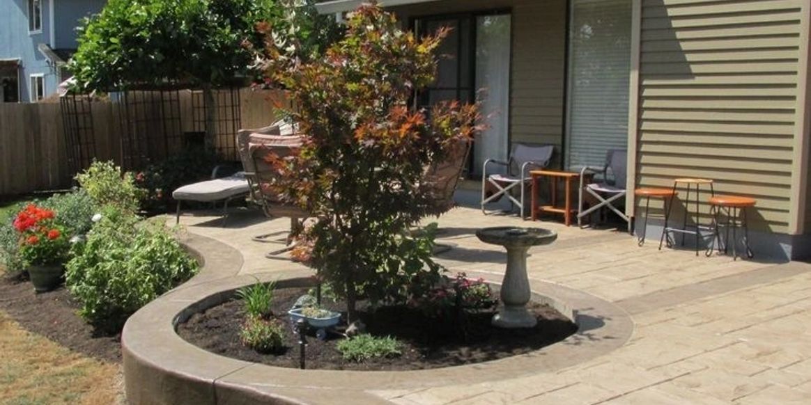 Backyard patio with circular planter, tree, potted plants, and chairs by a house wall