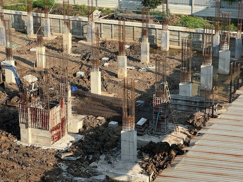 Construction site with concrete foundations, rebar columns, and piles of dirt under development
