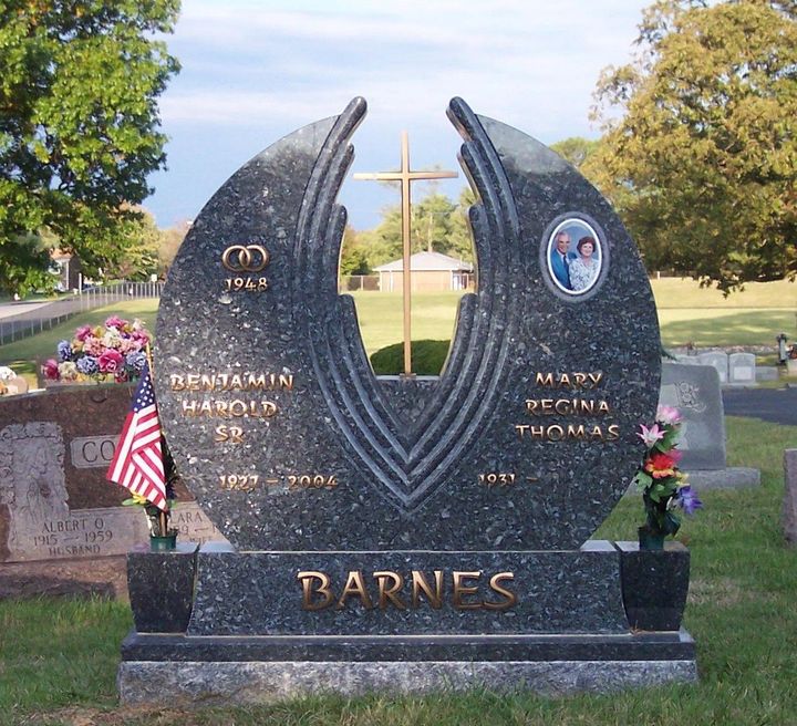 Barnes memorial headstone in a cemetery, with flags, flowers, and engraved emblems.