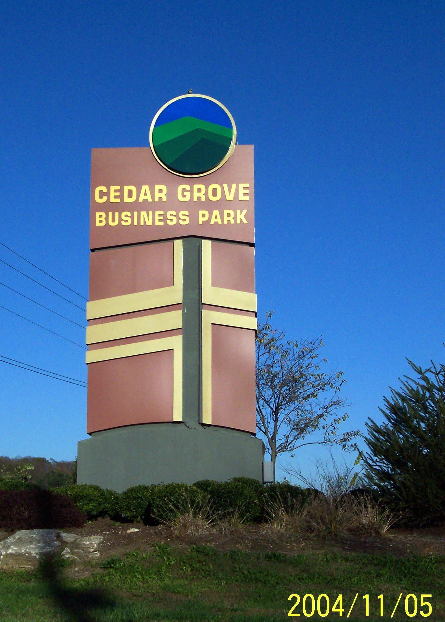 Cedar Grove Business Park sign on a tall tan pillar against a clear blue sky