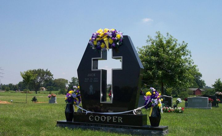 Black gravestone with white cross and flowers in a cemetery field, engraved "COOPER"