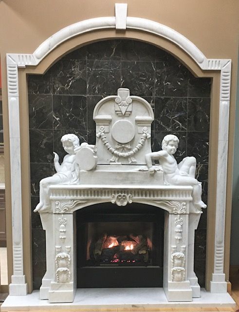 Ornate white fireplace mantel with cherubs and a lit fire against a dark tiled surround