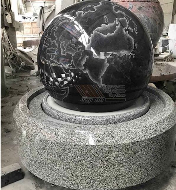 Black marble sphere being polished on a granite base in a workshop