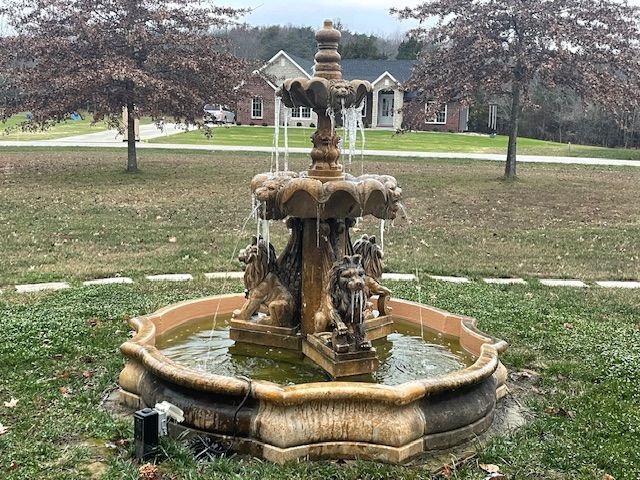 Ornate stone fountain on a grassy lawn with a house in the background