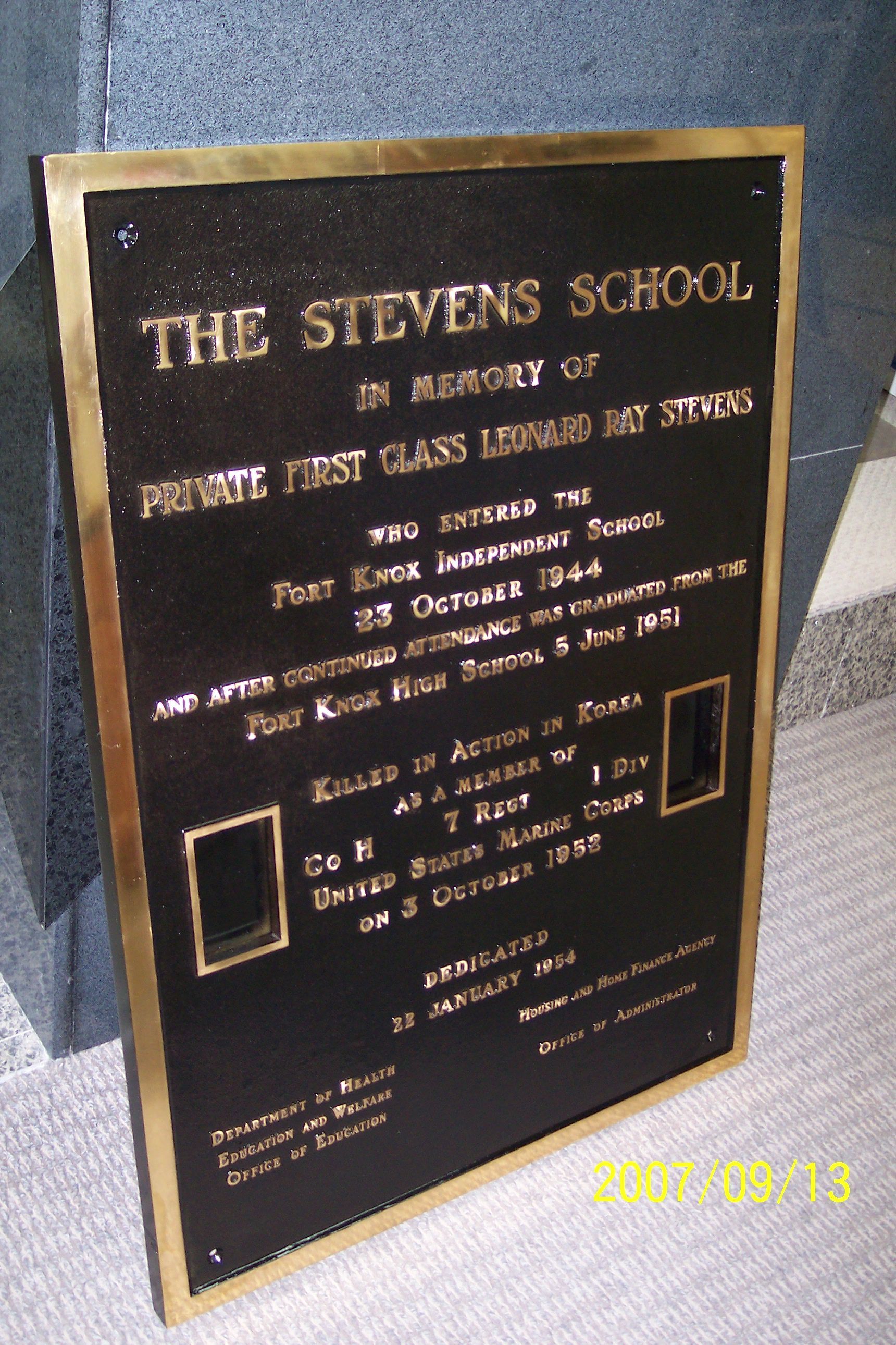 Plaque for The Stevens School memorial, black with gold lettering on a stone wall