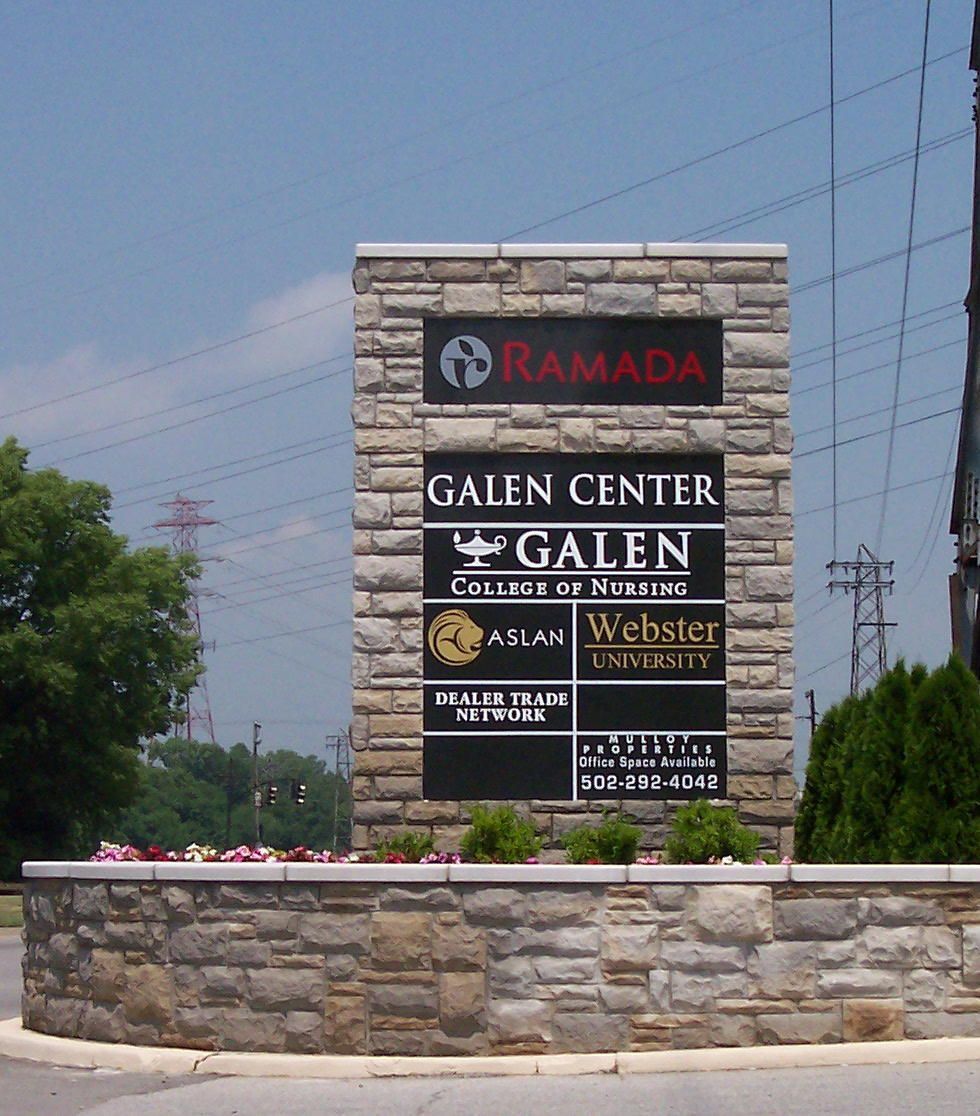 Stone monument sign for Ramada and Galen Center businesses by a roadside under a blue sky