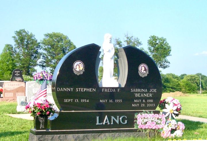 Black granite memorial gravestone with flowers and a white angel statue in a cemetery.